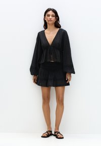 Costum două piese de culoare neagră, compus dintr-o bluză scurtă cu decolteu adânc în V și mâneci evazate, asortat cu o fustă mini evazată. Material ușor, texturat.