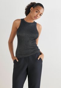 Zwarte mouwloze top met een geribbelde textuur en een slim fit, gecombineerd met hoge zwarte broeken. De stof heeft een subtiele glans.