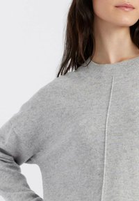 Grauer Pullover mit rundem Halsausschnitt, aus weichem, strukturiertem Material hergestellt. Verfügt über eine zentrale Naht auf der Vorderseite und lässige Ärmel.