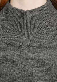 Šedý pletený svetr s vysokým žebrovaným límcem. Látka má měkkou texturu a jednotný vzor po celém povrchu.