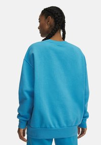 Blauw sweatshirt met ronde hals, ruime pasvorm en geribbelde manchetten. Zachte textuur en effen kleur zonder extra patronen of accenten.