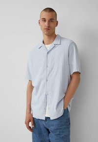 Lichtblauwe shirt met korte mouwen, van een textuurstof, met knopen aan de voorkant en een puntsluiting, gecombineerd met blauwe jeans.
