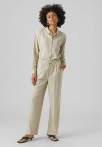 Chemise boutonnée beige clair avec une poche, associée à un pantalon beige ample avec une taille élastique. Tissu doux et coupe décontractée.
