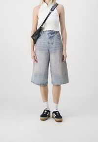 Denim culottes dengan pencucian pudar, pinggang tinggi, dan kaki lebar. Dipadukan dengan atasan tanpa lengan berwarna putih dan sepatu sneaker hitam dengan garis putih.