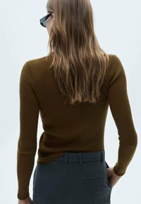 Haut à manches longues côtelé marron porté avec un pantalon gris foncé. Le tissu semble texturé, avec une coupe ajustée et une légère encolure arrondie à l'ourlet.