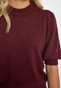 Burgundska pletena pulover s rebrastim ovratnikom, kratkimi napihnjenimi rokavi, mehkobo in sproščenim krojem.