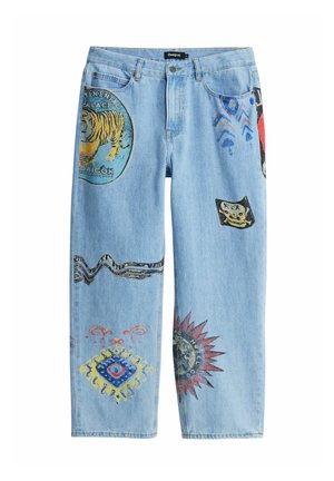 Jean en denim bleu clair avec des patchs graphiques colorés comprenant un tigre, un rayon de soleil, des formes abstraites et des motifs décoratifs.