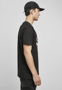 Camiseta de algodón negra de manga corta, con un estampado gráfico en el frente. Combinada con pantalones vaqueros oscuros y una gorra negra.