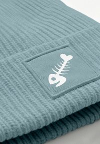 Knitted blue beanie with ribbed texture and a square fabric patch featuring a white fishbone graphic.