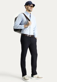 Camicia azzurra chiara, pantaloni blu navy, sneakers bianche con accenti verdi e beige, uno zaino scuro e un cappellino blu navy.