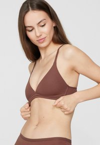 Sostén marrón con forma triangular, tirantes finos ajustables y una textura suave de tela. El diseño presenta un escote bajo y detalles mínimos de costuras.