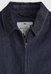 Col de veste en jean bleu foncé avec surpiqûres orange et devant partiellement zippé montrant l’étiquette Levi Strauss à l’intérieur.