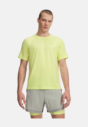 Homme portant un t-shirt de sport jaune clair à manches courtes et un short gris clair, debout avec les bras détendus devant un fond blanc.