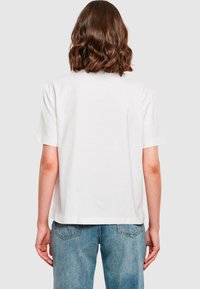 T-shirt bianco in cotone con maniche corte, vestibilità comoda e orlo dritto. Abbinato a jeans di denim azzurri chiari, con leggeri sbiadimenti.