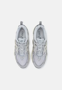 Adidași gri deschis cu un strat superior din plasă, detalii texturate, talpă intermediară albă moale și accente reflectorizante pe șireturi și călcâi.