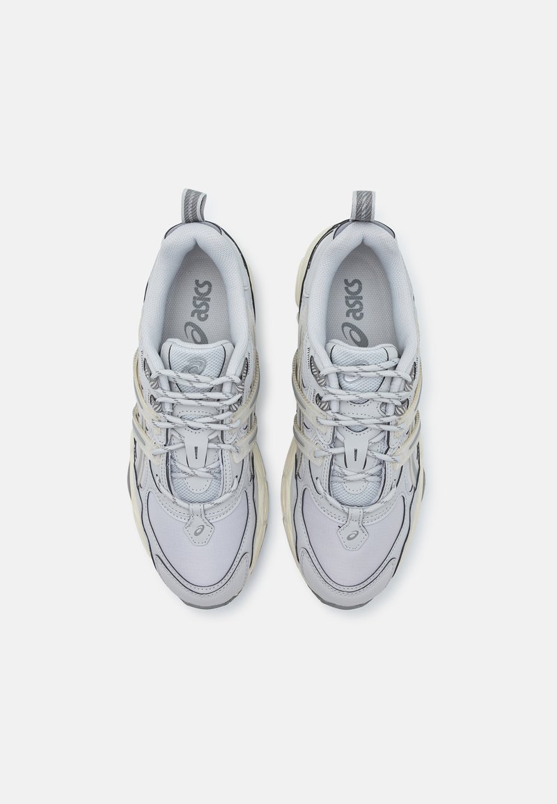 Hellgraue Sportschuhe mit einem Obermaterial aus Mesh, strukturierten Details, einer weichen, weißen Zwischensohle und reflektierenden Akzenten an den Schnürsenkeln und der Ferse.