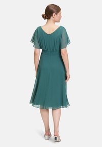 Grünes Chiffonkleid mit kurzen, flatternden Ärmeln, einer taillierten Taille und einem ausgestellten Rock. Rückenreißverschluss und glatte Textur.