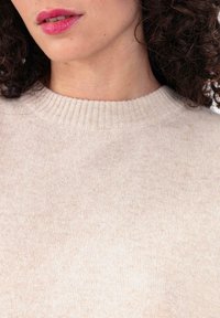 Pull en maille beige avec un col côtelé. Texture douce, coupe ajustée et légère variation de couleur partout.