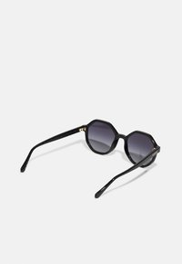 Μαύρα οκταγωνικά γυαλιά ηλίου με γκρίζους φακούς κλίσης. Γυαλιστερή επιφάνεια, υφασμάτινα μαύρα μπράτσα και χρυσές λεπτομέρειες στη σκελετό.