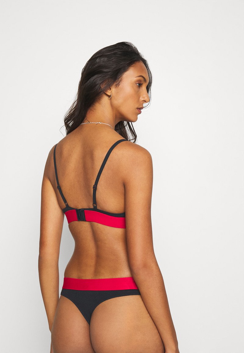 Conjunto de lencería negra con tirantes ajustables, una banda roja en la parte posterior y un tanga a juego con detalles en rojo y un diseño minimalista.