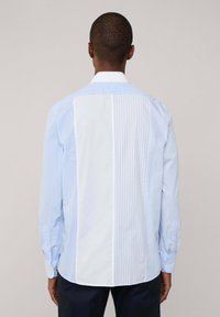 Camicia con bottoni caratterizzata da una combinazione di un solido azzurro chiaro e motivi a righe verticali blu, con maniche lunghe e colletto classico.