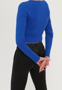 Prążkowany niebieski crop top z długimi rękawami, o dopasowanym kroju. Noszony z czarnymi, wysokim stanem spodniami, podkreślającymi smukłą sylwetkę.