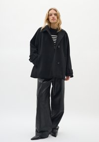 Oversized black wool coat with large buttons and side pockets, worn over a black-and-white striped top. Paired with black leather wide-leg pants.
