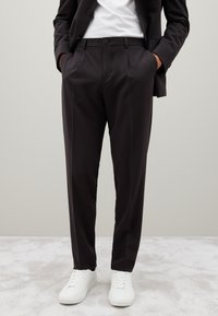 Donker op maat gemaakte broeken met een slim fit, met een gladde textuur en subtiele plooidetails, gecombineerd met witte sneakers.