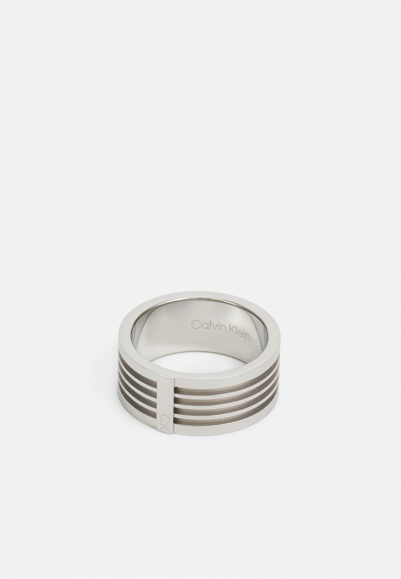 Stainless steel ring featuring a smooth finish with horizontal grooves and a small integrated accent. Engraved brand name inside.
