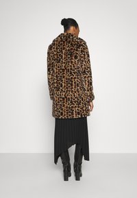 Leopardmönstrad pälsjacka med krage, medellång design och mjuk textur, i kombination med en svart plisserad kjol och knähöga stövlar.