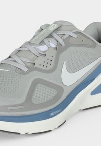 Ανοιχτό γκρι αθλητικό παπούτσι Nike με λευκό σύμβολο Swoosh, μπλε μεσαία σόλα, πλέγματα και γκρι κορδόνια. Κείμενο "Nike React X" στη μεσαία σόλα.