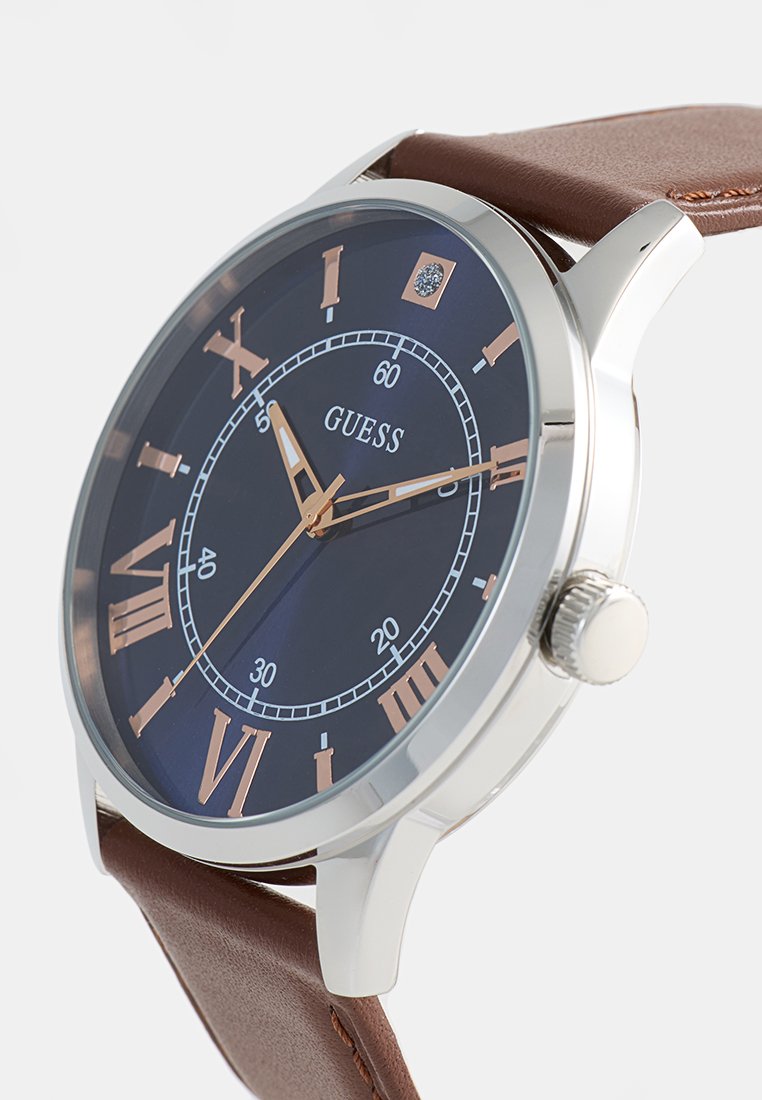 Braunlederarmbanduhr mit einem runden Gehäuse aus Silber, einem dunkelblauen Zifferblatt, roségoldenen römischen Ziffern und einem subtilen strukturierten Detail.