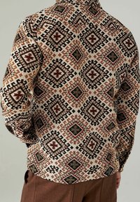 Camicia a maniche lunghe in tessuto beige con un motivo geometrico in diamanti rossi, neri e marroni, accentuato da zigzag. Include polsini con bottone.