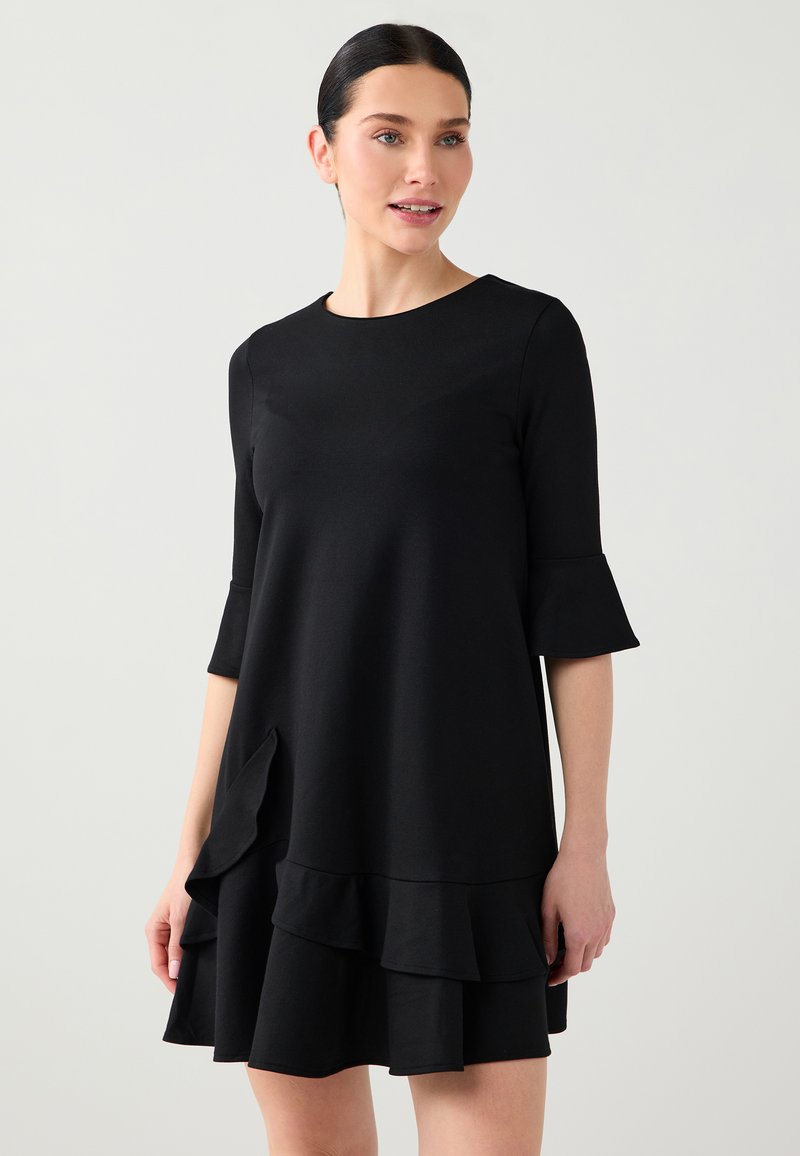 Robe noire avec manches évasées trois-quarts, encolure arrondie et ourlet à volants superposés. Réalisée dans un tissu lisse et extensible.