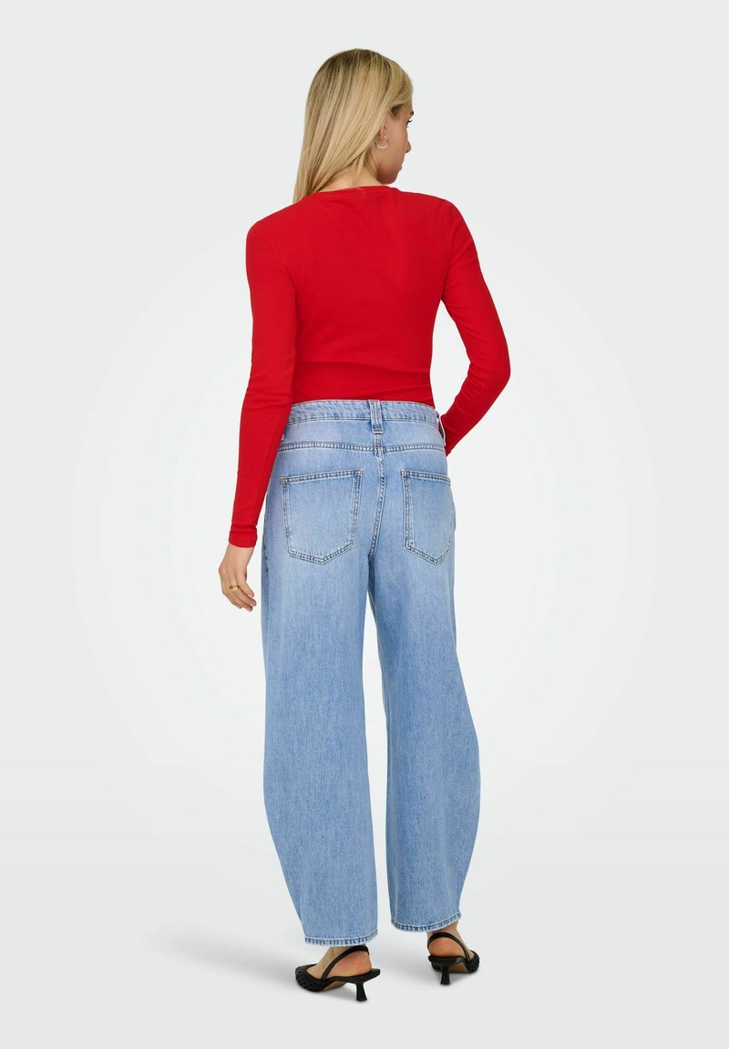 Top rojo de manga larga combinado con jeans de tiro alto de pierna ancha en azul claro. Los jeans tienen un ligero desgaste y dos bolsillos traseros. Sandalias negras de tacón alto.