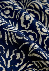 Marineblauer Stoff mit komplizierten weißen Blumen- und Blattmustern, der eine glatte Textur und einen subtilen Glanz für zusätzliche Tiefe aufweist.