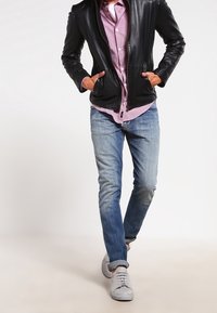 Černá kožená bunda přes světle růžovou kostkovanou košili, nošena s světle modrými džíny a bílými teniskami. Bunda má zip vpředu a dvě kapsy.