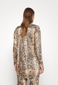 Långärmad topp i ormskinnsmönster, med en blandning av bruna, beige och vita nyanser, med en slät textur och knappslut.