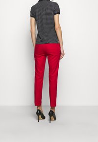 Černo-bílý pruhovaný polo shirt s krátkým rukávem v kombinaci s červenými těsnými kalhotami a černými lodičkami, z pohledu zezadu.