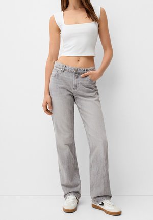 Jean en denim gris clair avec une coupe droite, fermeture à bouton et poches avant. Associé à un crop top blanc ajusté à encolure carrée.