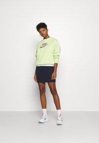 Sweat-shirt vert clair avec un logo Nike à motif léopard, associé à une mini-jupe navy et des baskets blanches à accents colorés.