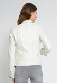 Weiße Lederjacke mit taillierter Passform, subtilen Nähdetails und verstellbaren Manschettenriemen. Glatte Textur mit einem klaren, modernen Look.