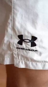 Valged sportlikud lühikesed püksid, mille ääres on must tikitud Under Armouri logo. Materjal näeb välja kerge ja siledana.