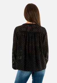 Blusa negra con un tejido texturizado y transparente adornado con pequeños brillantes blancos. Corte holgado con un detalle fruncido en la parte posterior.