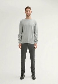 Világosszürke, kerek nyakú pulóver hosszú ujjakkal, sötétszürke nadrággal kombinálva. A modell egyenesen áll, fekete cipőt visel. Egyszerű, minimalista dizájn.