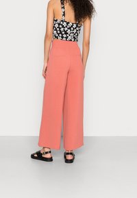 Breda, korallfärgade byxor i texturerad tyg med bakfickor. Matchas med en svart blommig crop top och svarta sandaler.