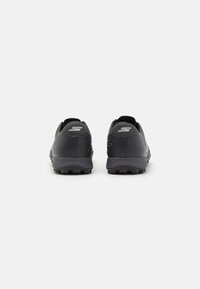 Chaussures de sport noires avec une tige synthétique lisse et texturée. Les caractéristiques notables incluent une coupe basse, une languette à l'arrière et une semelle extérieure en caoutchouc à motifs.