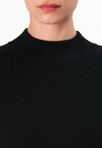 Svart strikket genser med høy ribbestrikket krage. Myk tekstur med en tettsittende design, som fremhever rene linjer og sømløs konstruksjon.