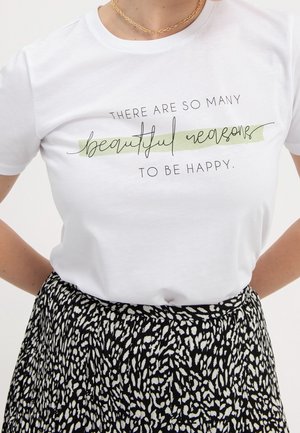 Wit overhemd met de tekst "Er zijn zoveel mooie redenen om gelukkig te zijn", gecombineerd met een zwart-wit patroon rok en een gouden ketting.