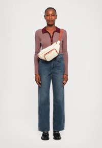 Beige Umhängetasche mit orangefarbenen Akzenten, weiche Textur; lang�ärmliges lila Oberteil mit bordeauxfarbenem Kragen; weit geschnittene blaue Jeans; schwarze Schuhe.